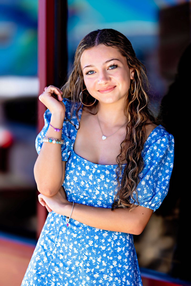 Teen girl posing in a blue floral dress with hoop earrings during a vibrant senior photography session in Orlando, Florida.
