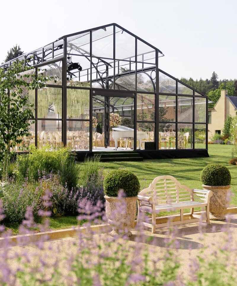 An aerial view of a glass marquee on a lawn with a long walkway and flowers at the entrance for Amelia and Olly Murs