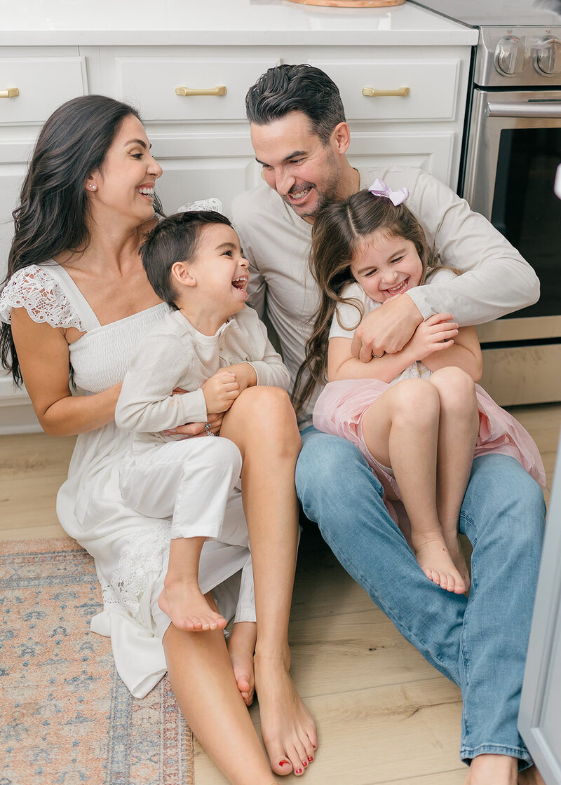 Mom and dad sitting on the kitchen floor tickling kids