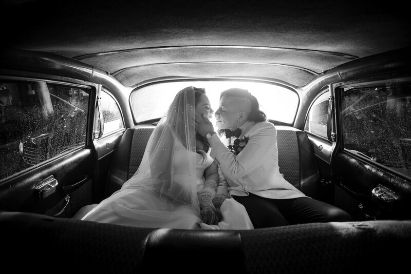A wedding couple sitting in the back of a car about to kiss.