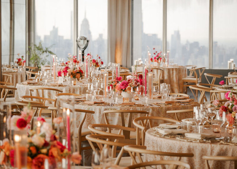 An elegant sunset wedding reception in New York, NY, with floral arrangements in shades of pink and orange, candlelit tables, and a breathtaking skyline view of Manhattan.