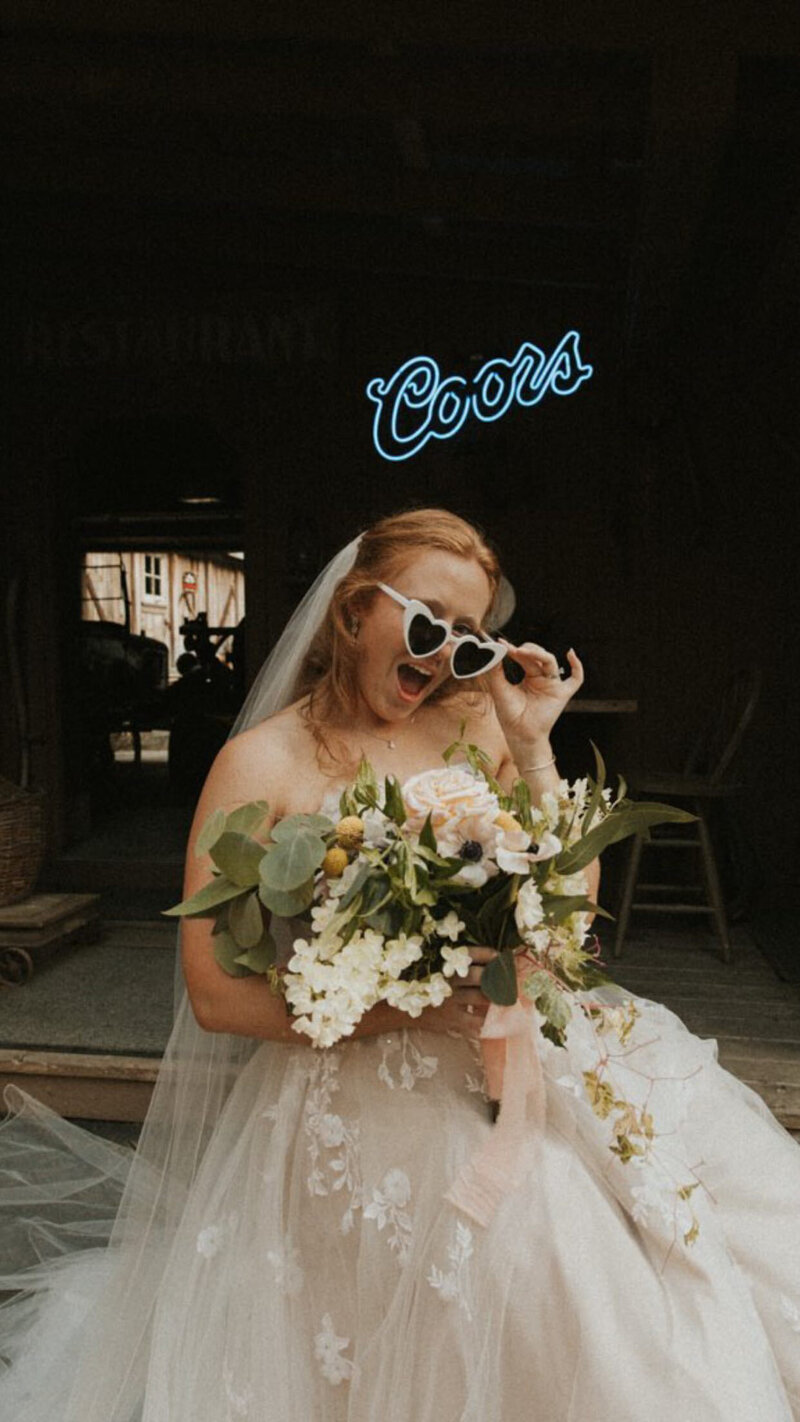 Bride stands and smiles with heart shaped sunglasses