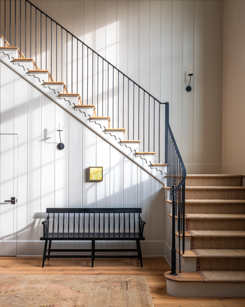 A timeless staircase design featuring warm wood treads, iron railing, and impressive paneling details. The contrast of black balusters against natural wood creates a balanced, modern-traditional aesthetic. Flooded with natural light, this entryway embodies a seamless blend of function and style.