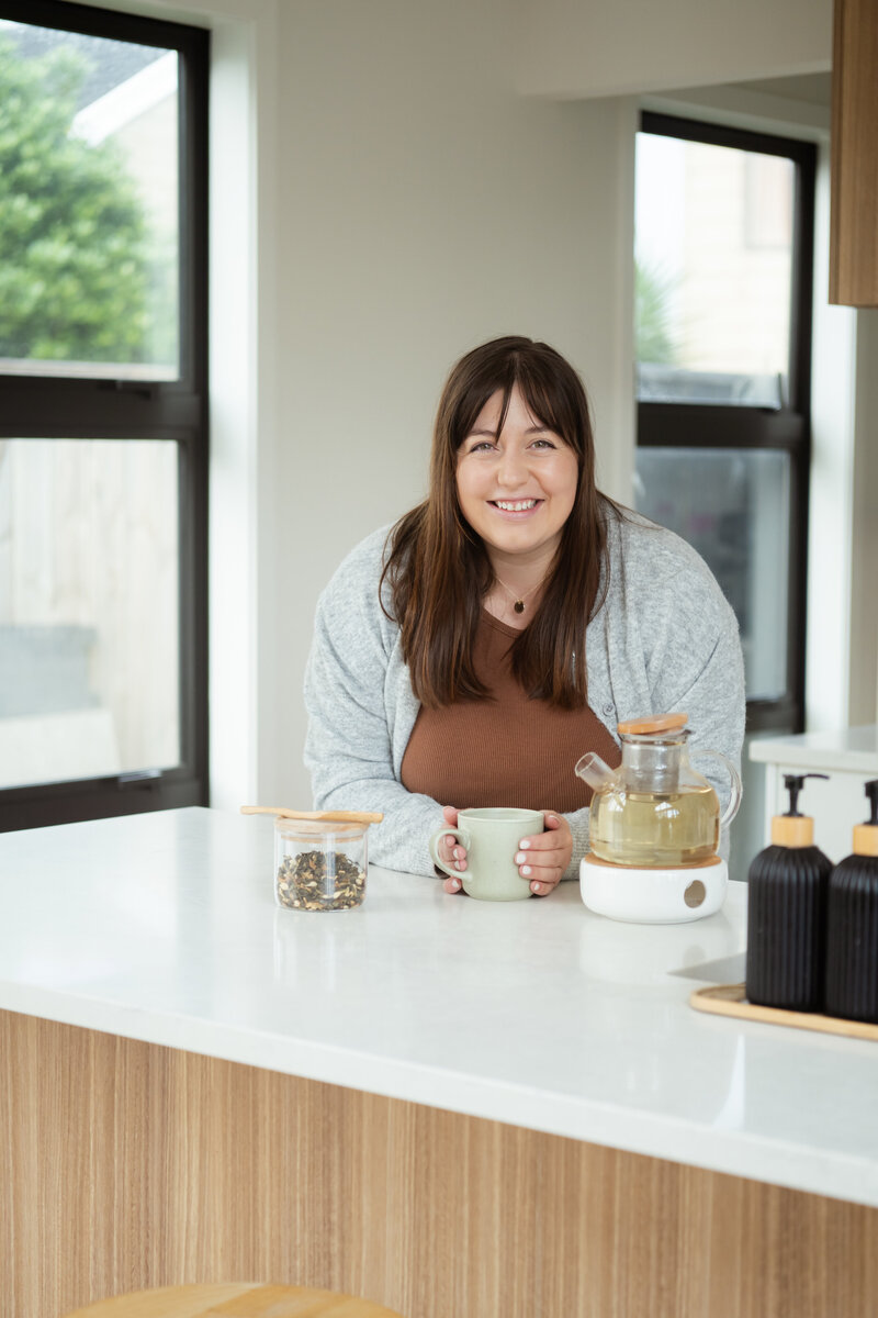 Chantal Hewitt smiling in brown shirt and grey sweater at kitchen island with a green mug - Family Autism Support Coach at Chantal Hewitt Coaching1
