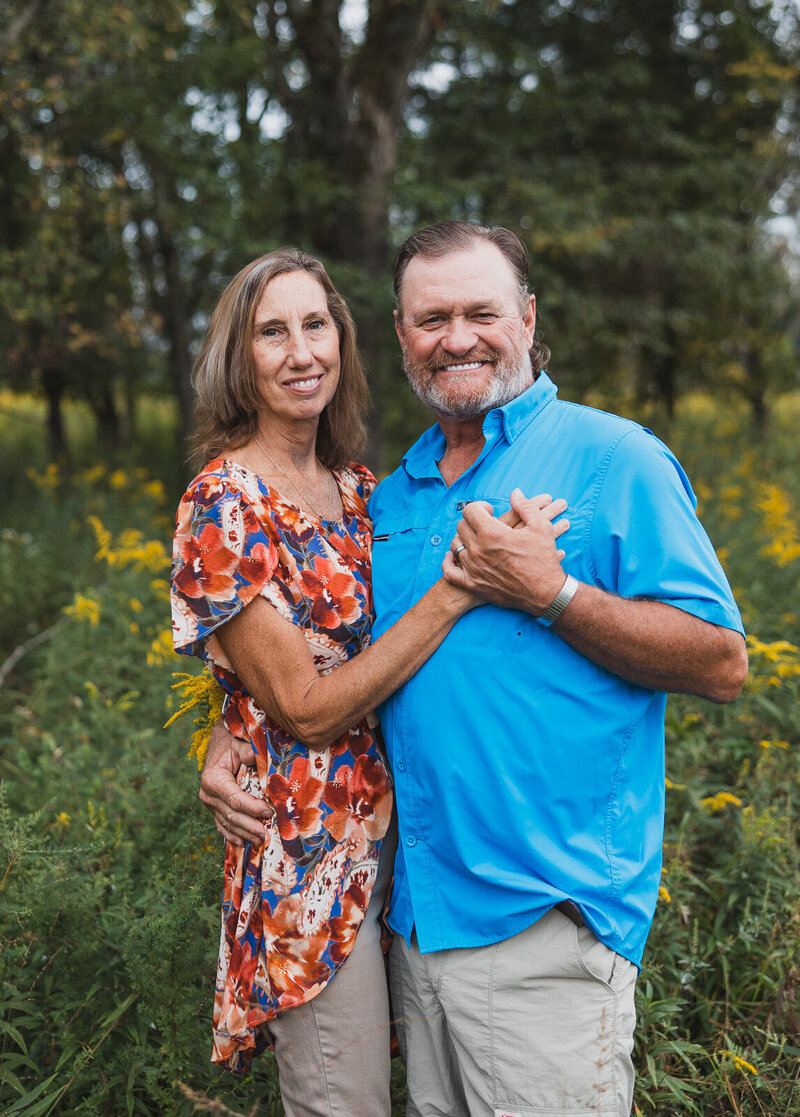 Couple standing close, hugging and holding hands and standing in a field of flowers in Farmington, Missouri. 