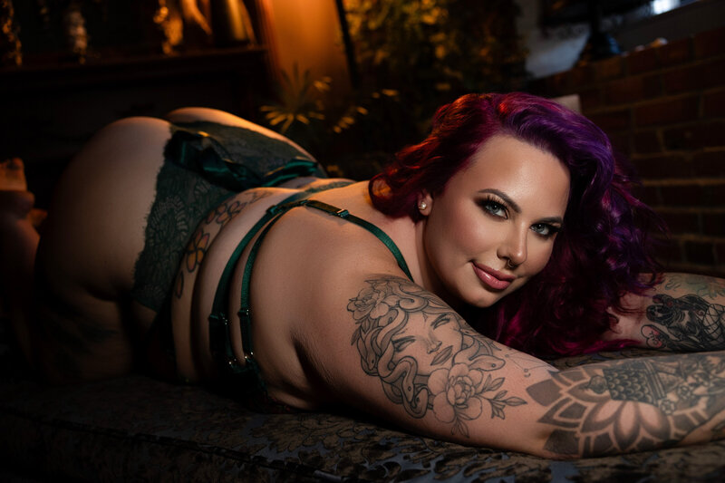 A woman smiles while laying across the floor in lingerie with purple hair
