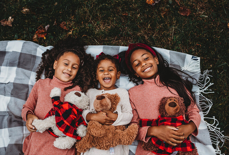 Family photographers Maryland captures sibling photo with three sisters laying together with their teddy bears on a blanket in a park