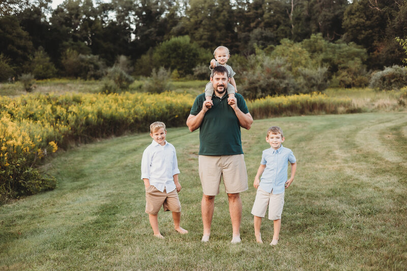 dad holding a little boy on his shoulders and his older two sons standing on either side of him for a family photo