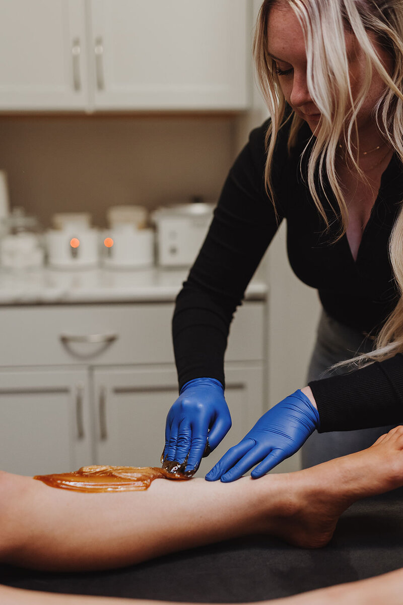 Female esthetician uses sugar wax to remove hair from client's leg