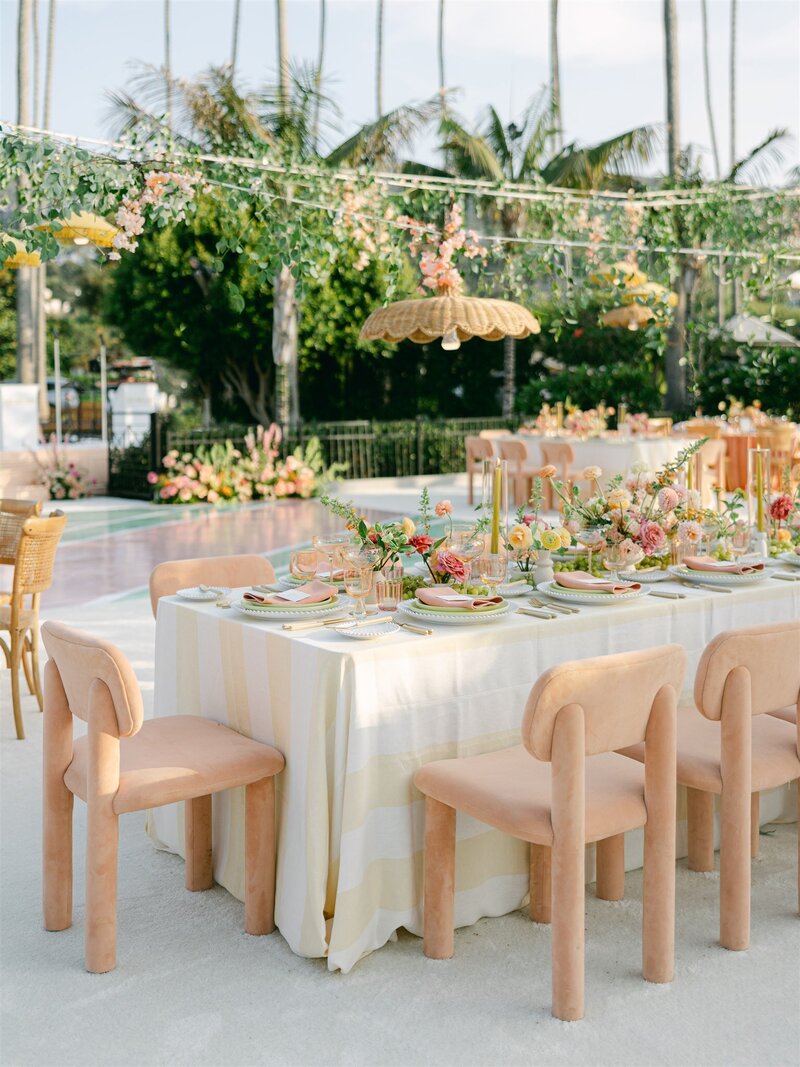 Our Mellow Dining Chair in peach at a table with a linen and a stunning tablescape with our rentals from Catalog and our Scalloped Rattan Lights hanging above. 