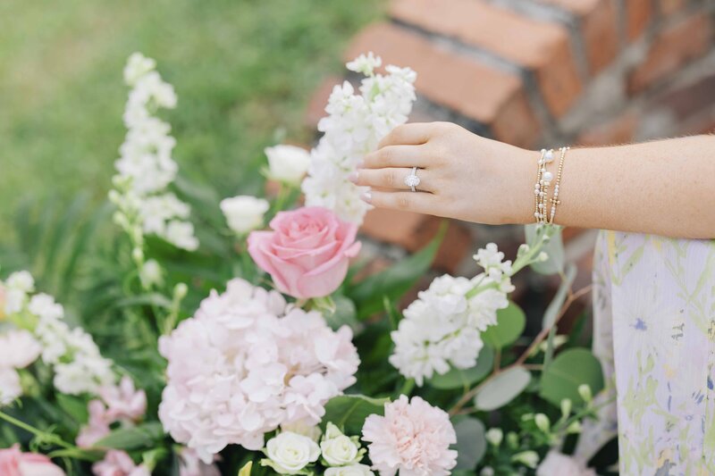 a woman's hand with an engagement ring touching a flower bush
