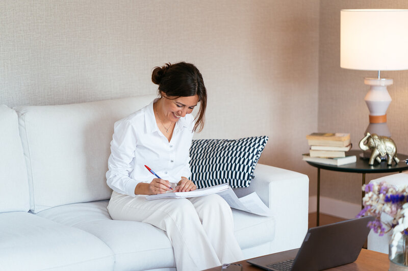 Female entrepreneur sitting on a couch with a laptop and pen.