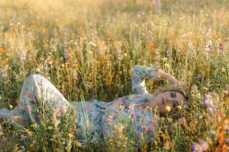 Woman in a floral power suit with bright blue eyeshadow crouched near a laundromat, exuding editorial flair — Greenville SC branding photography by Dani Lacey.