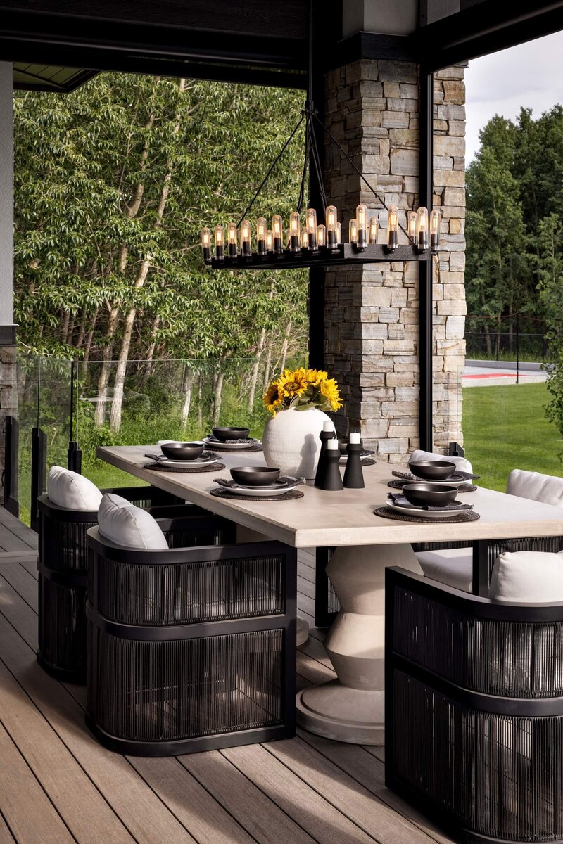 A glamorous outdoor dining space with curved rattan chairs, concrete dining table and oversized light fixture. 