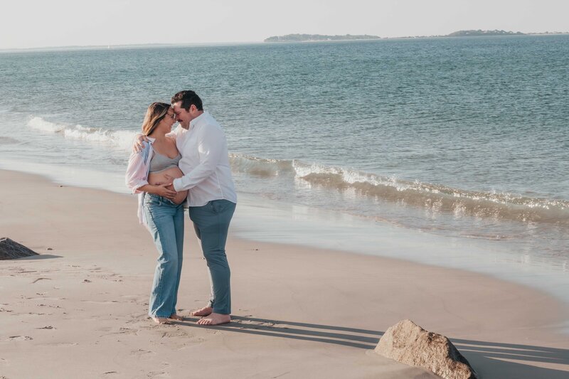 Husband and pregnant wife posing on beach for maternity photoshoot.