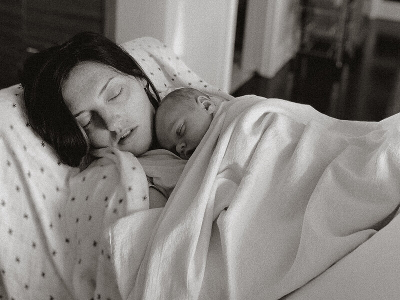 Intimate newborn moment: new mom asleep with baby on chest in soft light, storytelling family photography