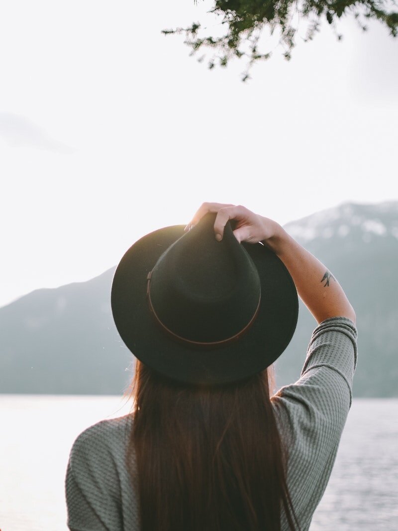 Woman in hat with her back to camera looking off into the sun rising over the sea or a lake