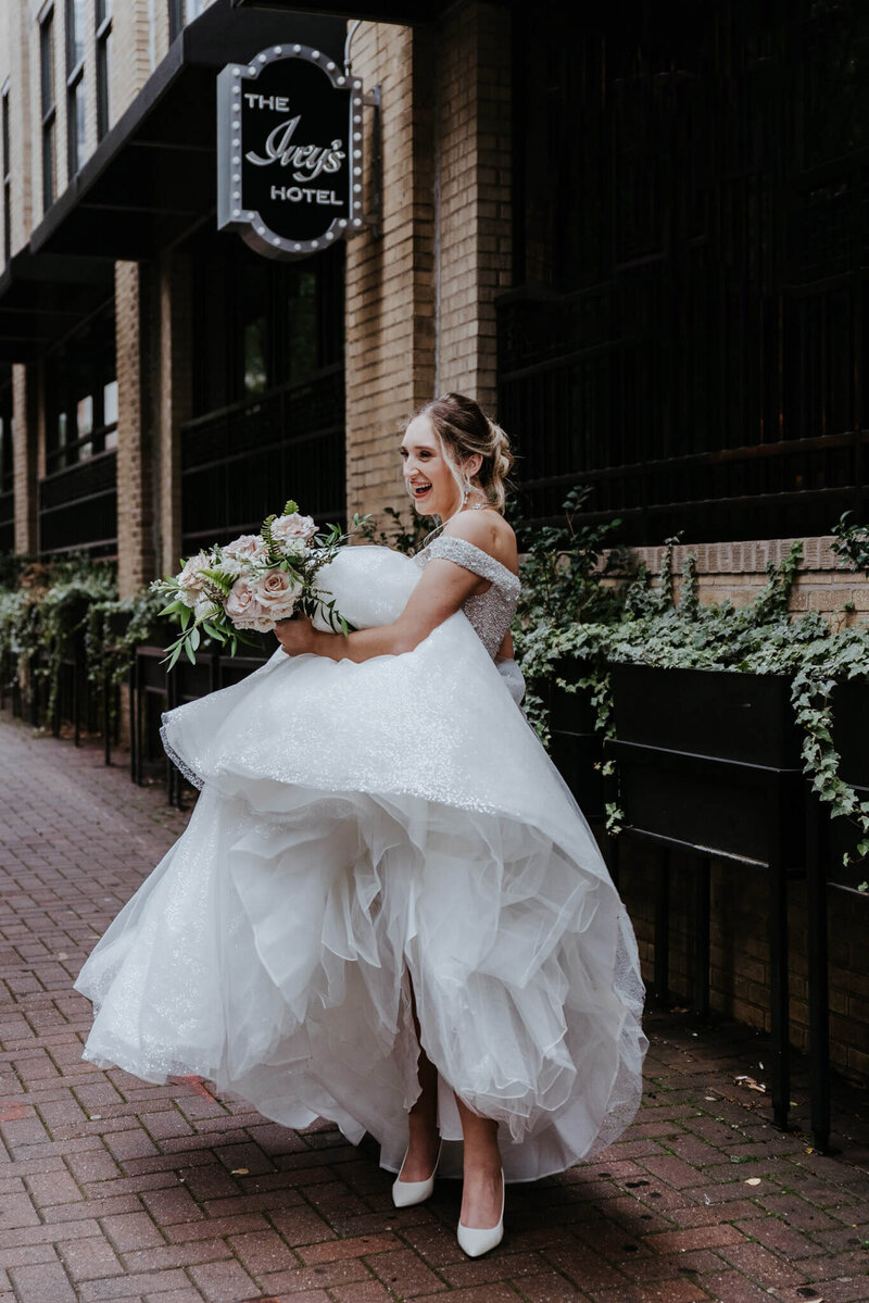 bride in downtown charlotte nc holding dress and standing by Iveys Hotel