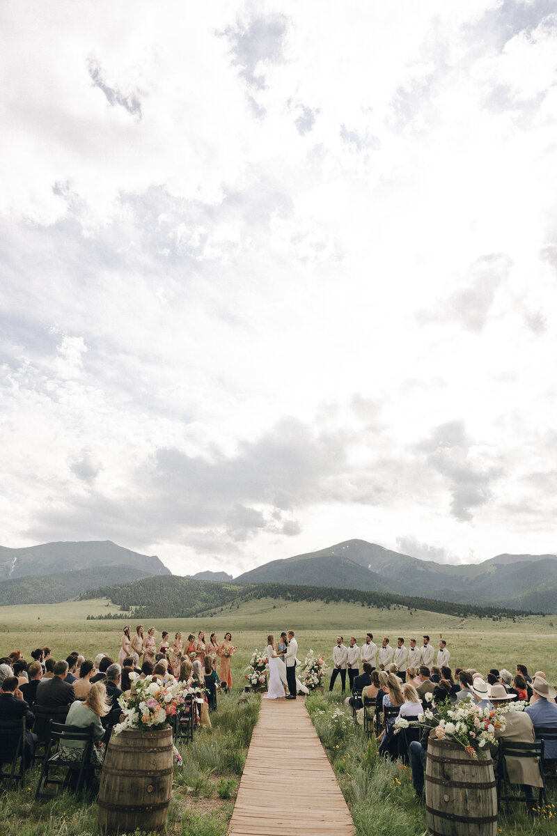 bride and groom standing an end of wedding aisle surrounded by wedding guests and bridal party