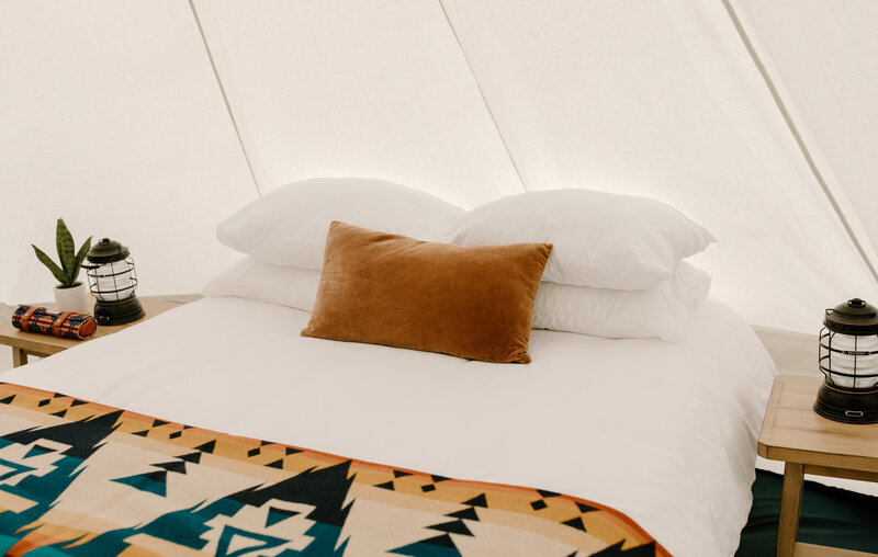 Close up full size bed white linens with multicolor Pendleton Blanket and velvet throw pillow