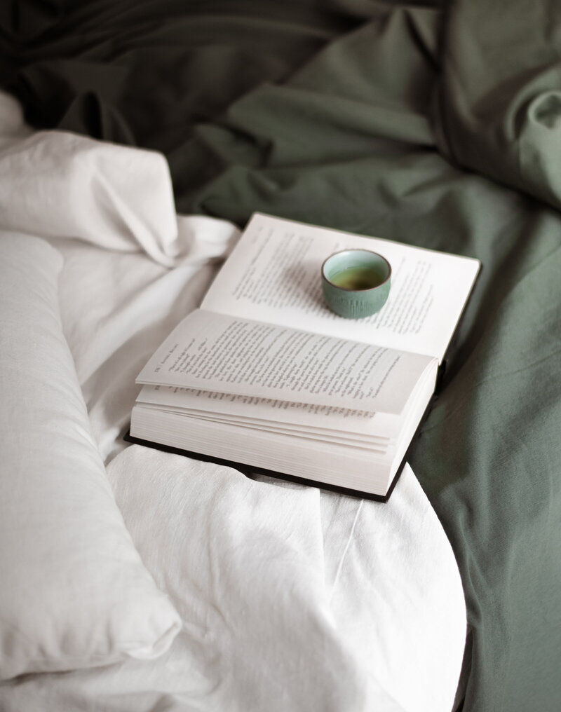 green bed with white comforter and book laying on top with coffee
