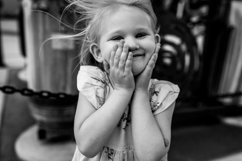 black and white image of little girl smiling with her hands on her cheeks. Photo by Portland Oregon Family Photographer.