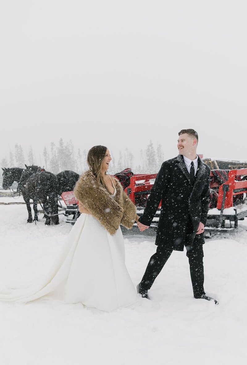 Bride and groom holding hands in the snow during their sleigh ride elopement in Winter Park, Colorado
