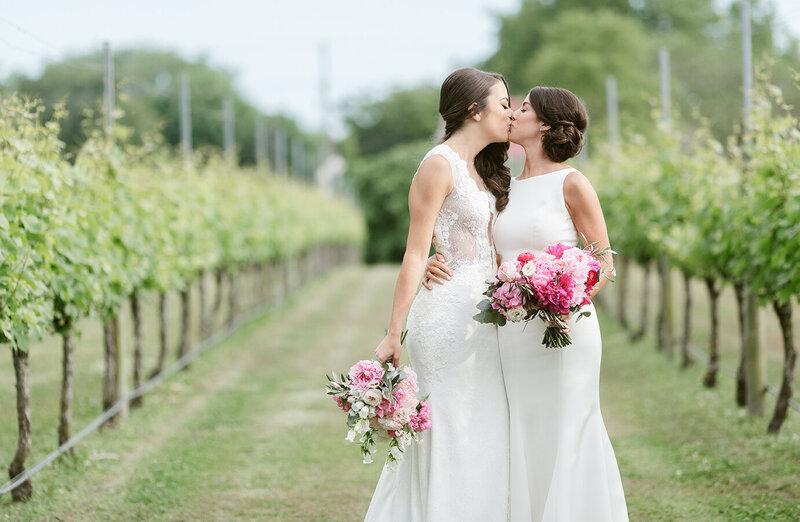 LGBTQ brides kissing in a lush vineyard