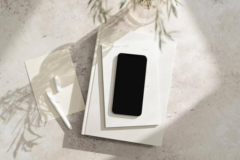 white travertine table with green plant, white notepads with iphone