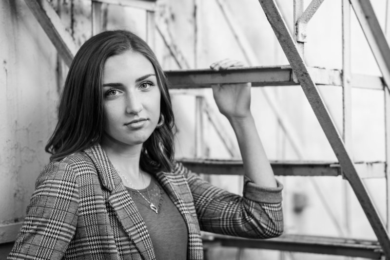 waynedale high school senior girl, standing under metal steps with hand on one step, standing off a little from camera looking over shoulder towards camera with serious face, black and white photo, photographed by jamie lynette photography canton senior photographer