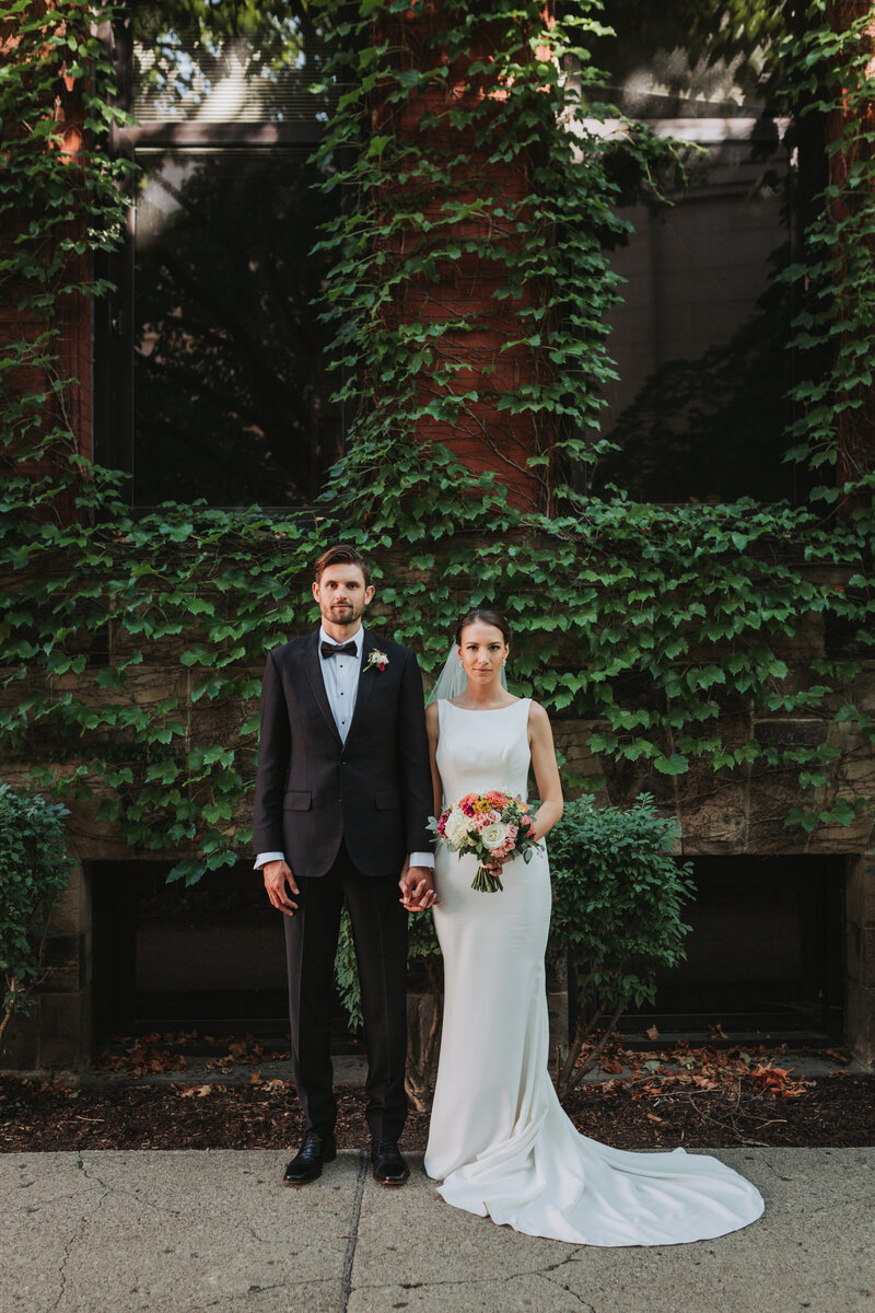 Portrait of bride and groom standing next to each other near an ivy wall