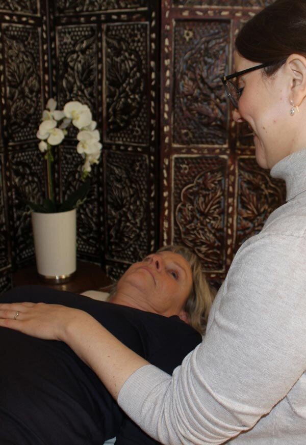 Kraniosakral behandling. Två personer som tittar på varandra i en behandling. händer berör solar plexuspå den liggande personen. 