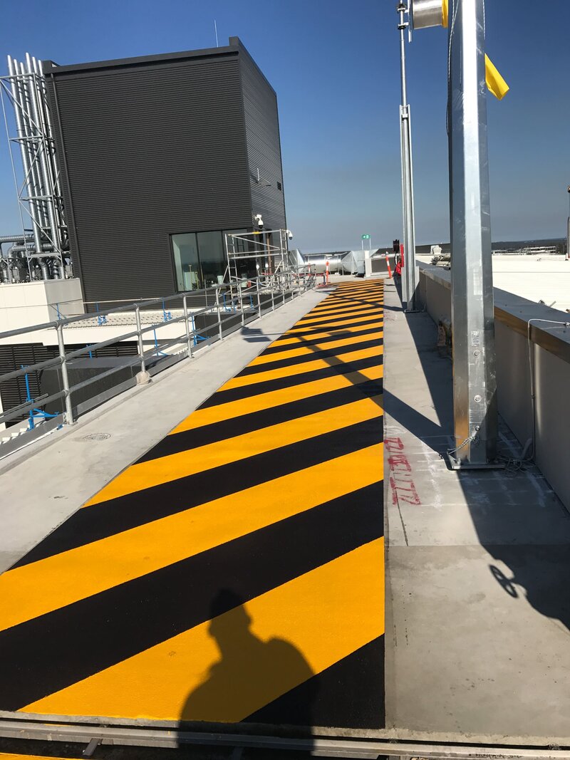 A yellow and black striped safety line marking walkway on the roof of a commercial building.