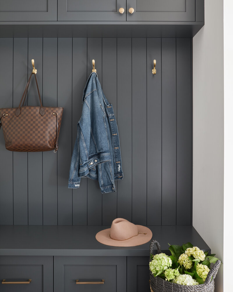 Panelled built-in foyer shelving and bench painted dark grey, there is a purse, jean jackets, and hat hanging up