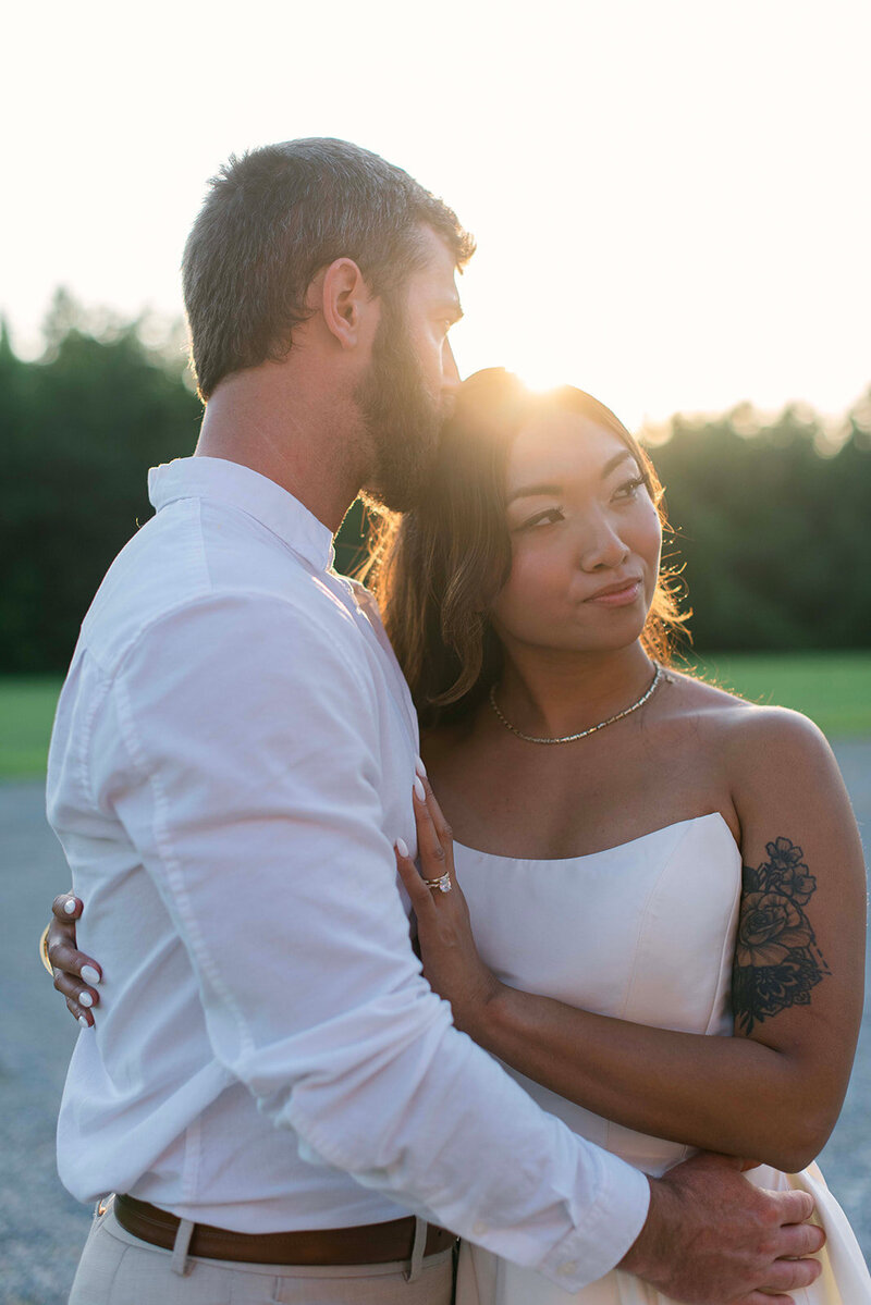 Stylistic image of groom kissing his bride's head while sunlight glistens between the couple