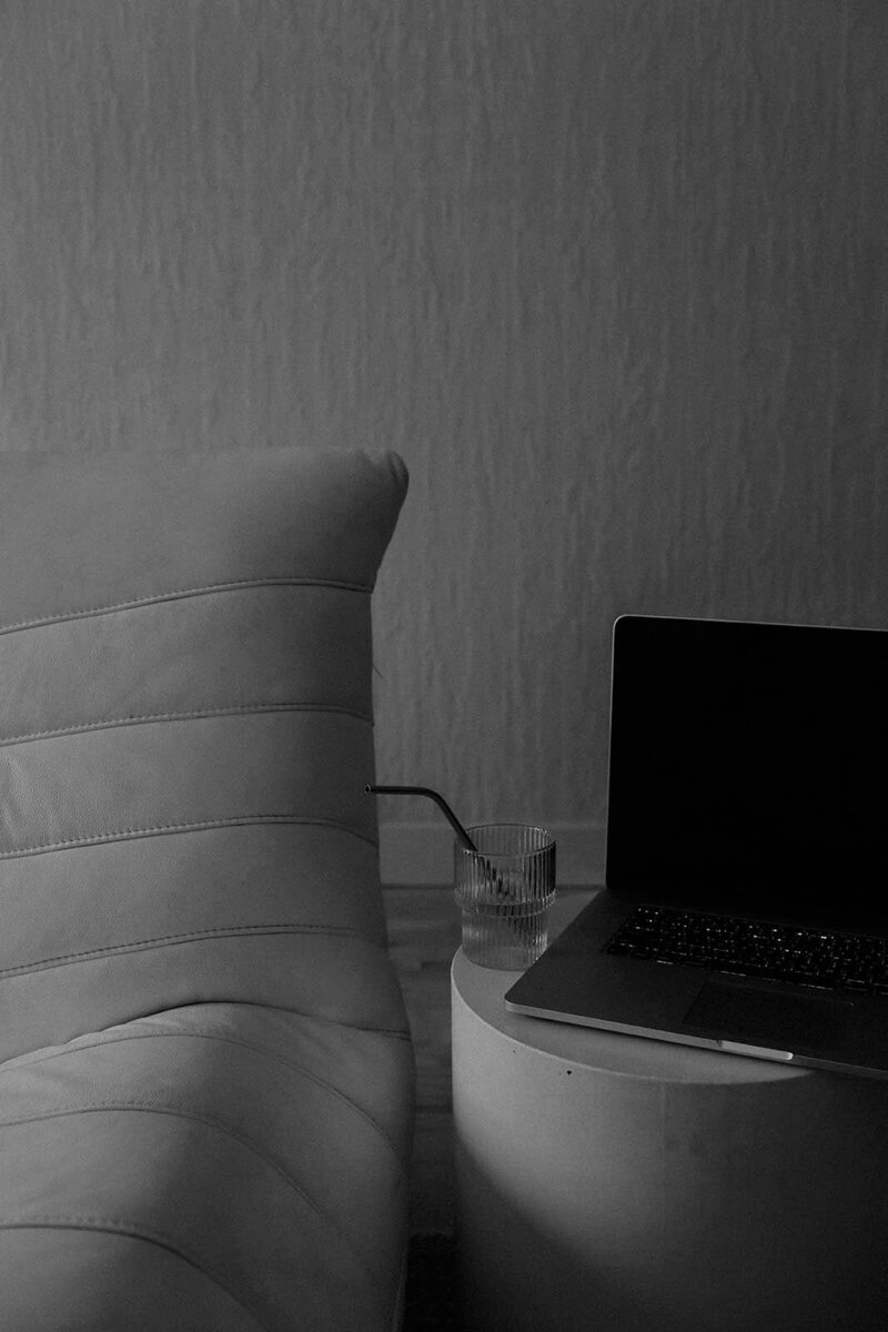 Lounge chair beside a water glass and closed laptop on a round table – represents calm, intentional design for The Aurum Effect section