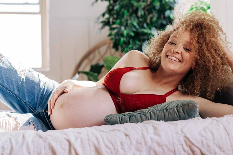 Maternity portrait of red haired woman in jeans and red lingerie