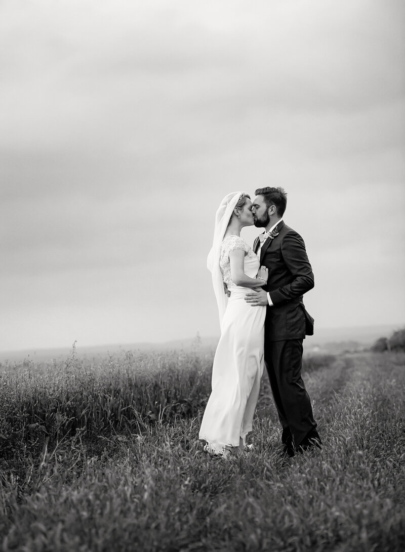 A romantic black and white image of a bride and groom kissing standing in a Texas Hill Country field
