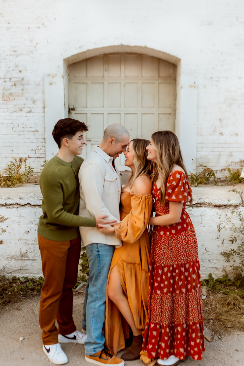 Photos of Mom and Dad snuggle each other while teenage kids hug on them during urban session with Maternity Kansas City Photographer.