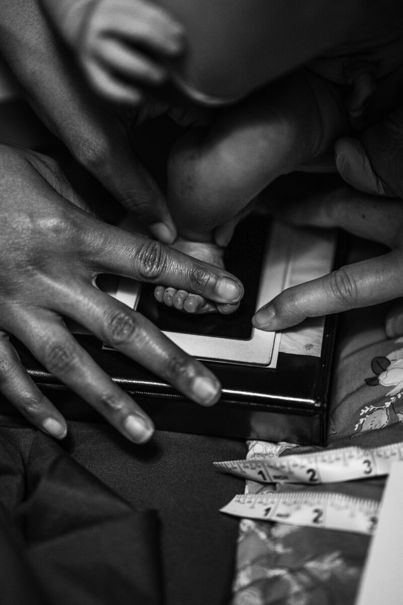 A black and white photo of a midwife pressing down a newborn baby's foot on an ink pad during its newborn exam
