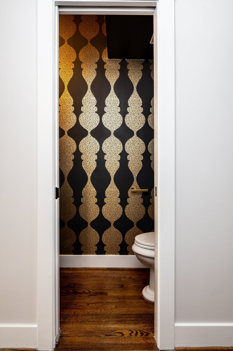 Hallway featuring bold, patterned wallpaper in black and gold, with white doors framing the entrance and a glimpse of a cozy room beyond