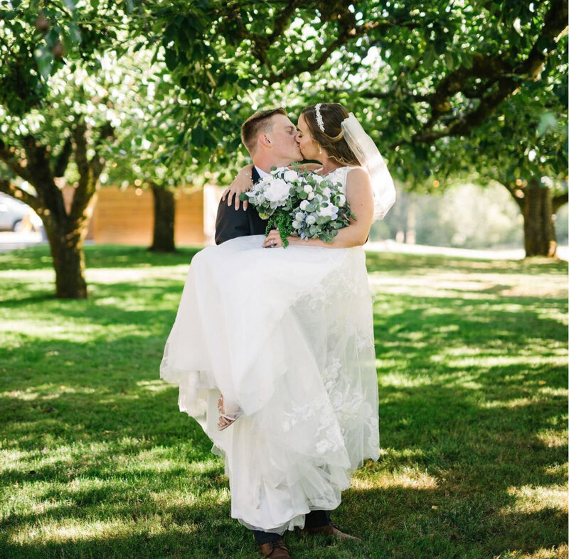 A groom carrying his bride under a canopy of trees
