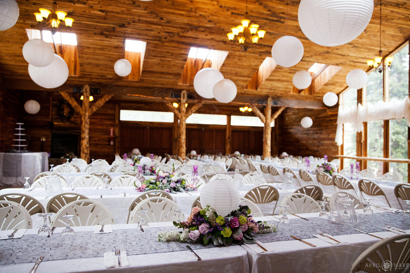 White tables with purple florals inside a barn wedding reception at Mountain View Ranch