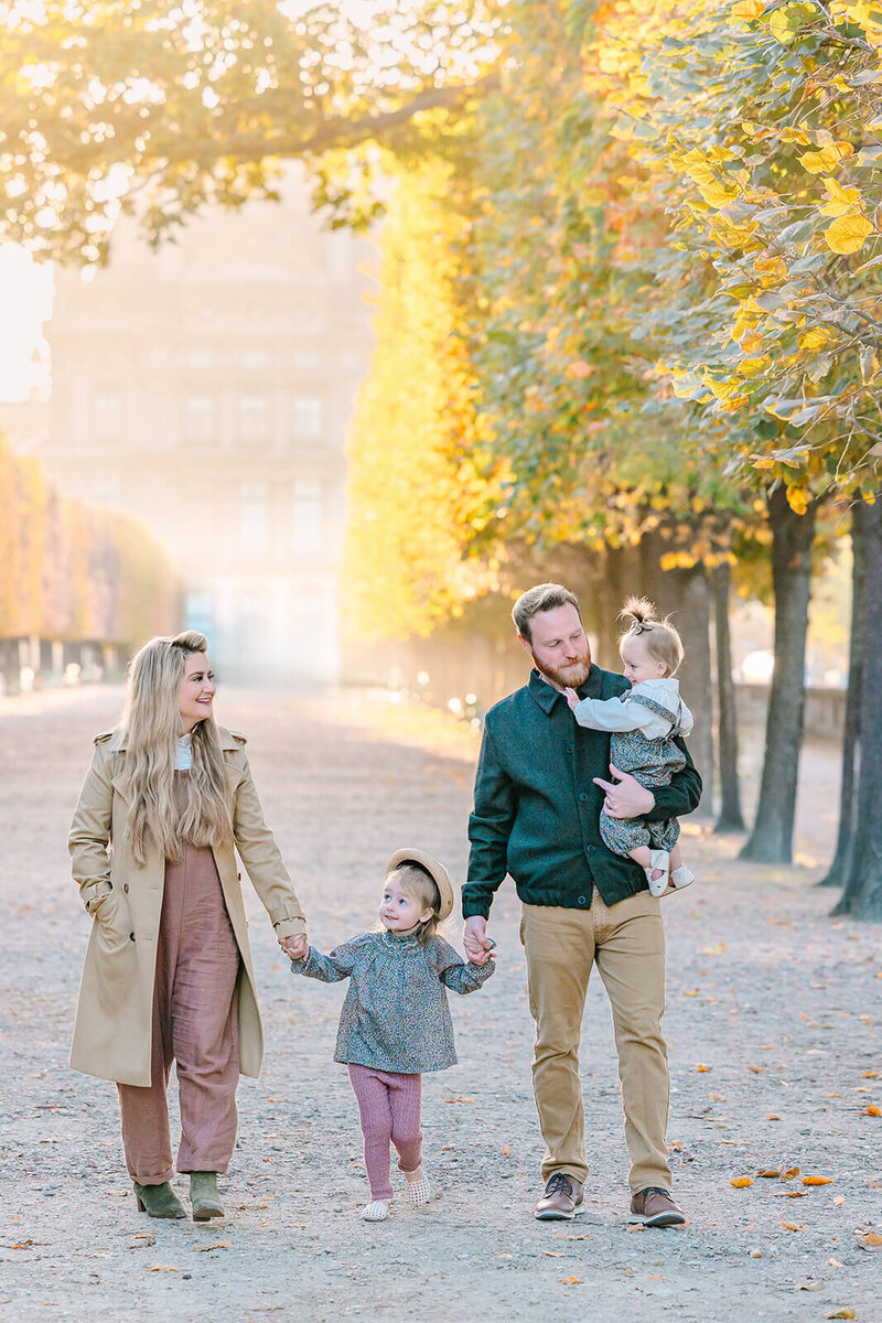 Family of four — mother, father, and two young children — walking together through the Louvre, Tuileries Garden, and Palais Royal during a Paris family photoshoot.