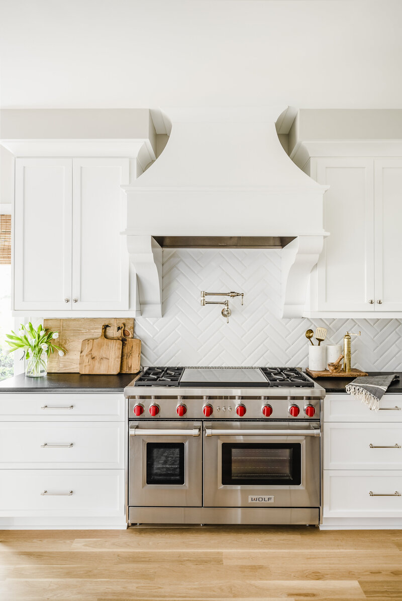 White kitchen with wolf range and herringbone white tile back splash.
