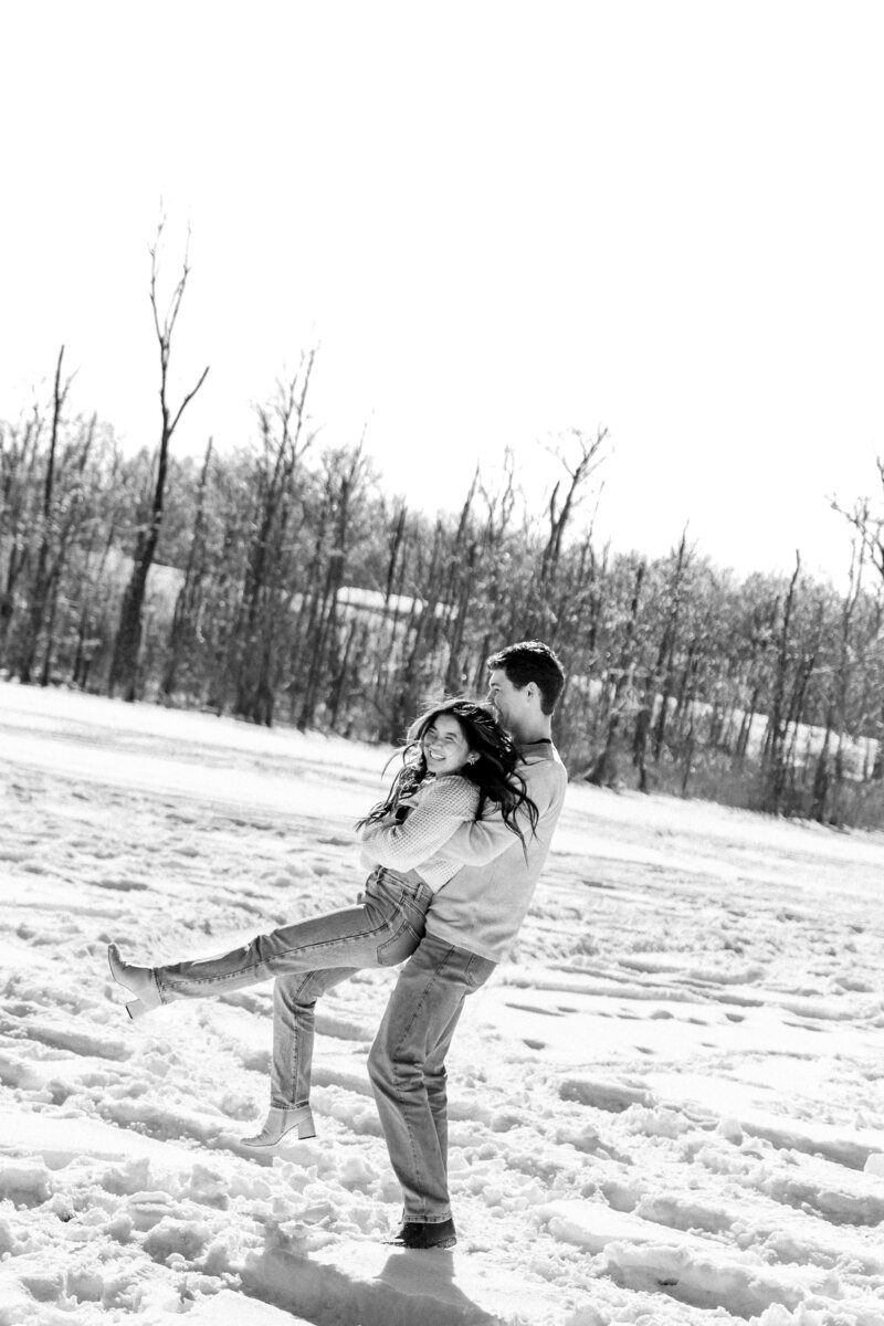 Couple captured in the woods during winter, with bare trees creating a serene, intimate atmosphere, showcasing their love in a quiet setting.