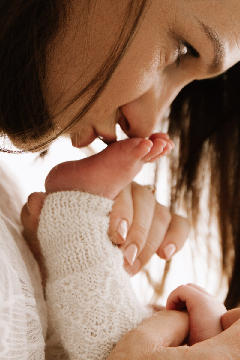 Mother kissing newborn baby’s tiny foot during intimate newborn photography session in Southwest Sydney studio
