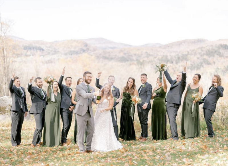 The bride, groom, and wedding party celebrating by popping a bottle of champagne with picturesque mountains in the background.