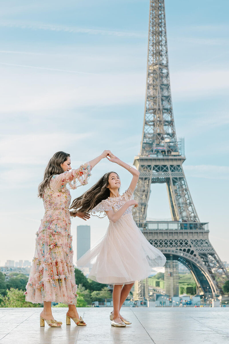 Mother and daughter dancing in dresses with the Eiffel Tower in the background at Trocadéro during a joyful Paris family photoshoot.