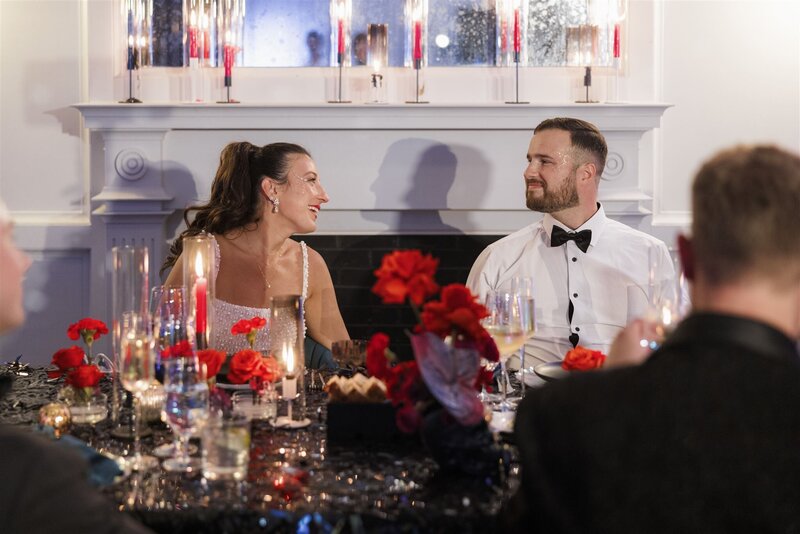 Bride and groom sitting at their head table in the ballroom of the Line Hotel DC talking to one another 